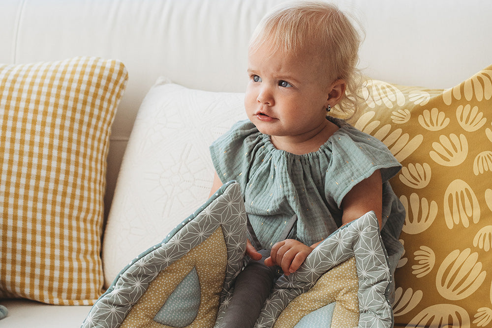 Baby sitting on a couch with patterned cushions and the liimmi butterfly